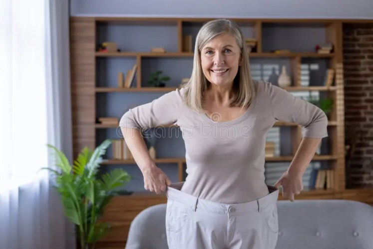 Happy mature woman showing her weight loss.