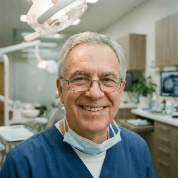 Dentist in blue scrubs sitting next to a dental chair in a clinic
